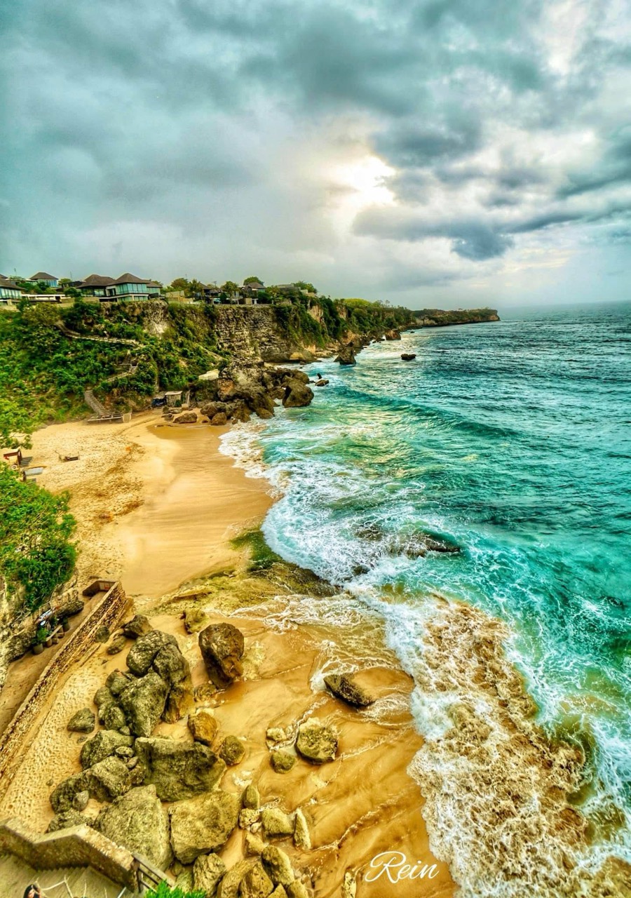 Pantai bertebing dengan ombak turquoise dan langit berawan